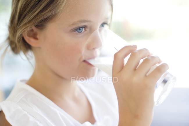 Età elementare ragazza bere latte da vetro . — Foto stock