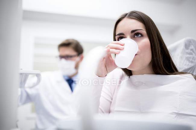 Paciente femenina bebiendo agua en clínica dental . - foto de stock