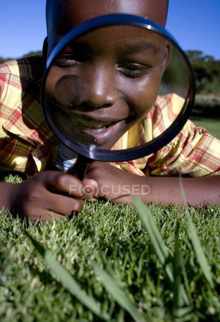Boy using magnifying glass on grass. — Stock Photo