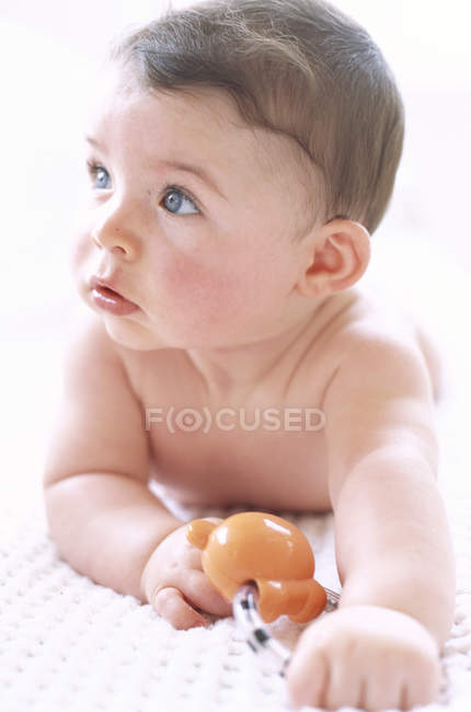 Baby boy lying on front and holding toy. — Stock Photo
