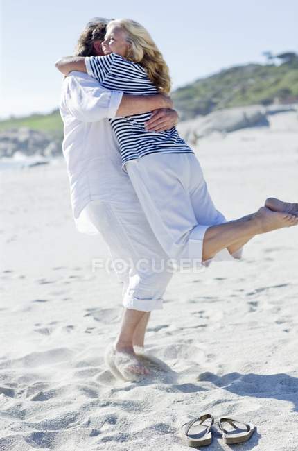 Mature couple embracing couple on beach. — Stock Photo