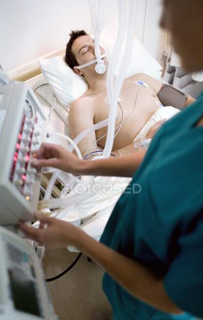 Enfermeira ajustando controles no ventilador ligado ao paciente inconsciente . — Fotografia de Stock