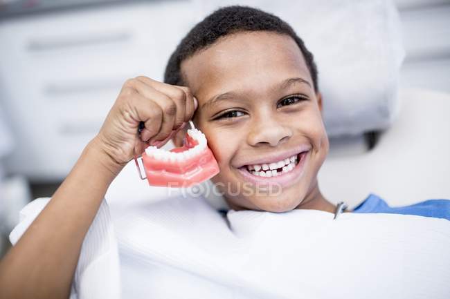 Retrato de niño sosteniendo dentaduras postizas y sonriendo . - foto de stock