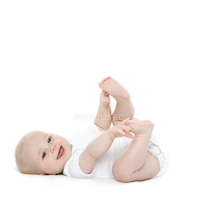 Baby boy lying on back and holding feet. — Stock Photo