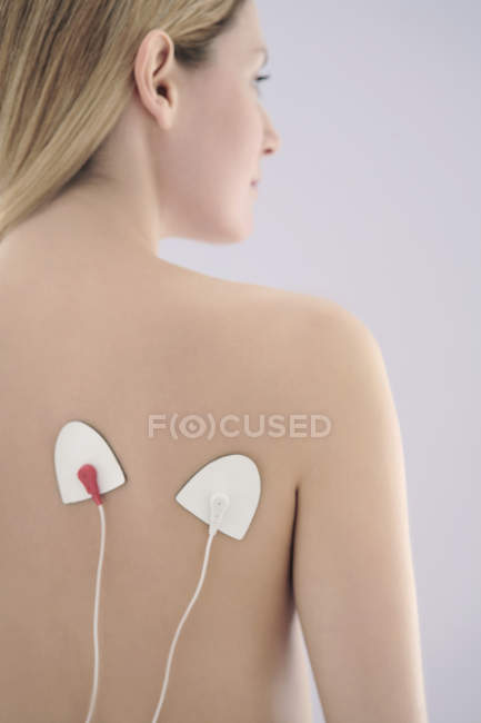 Mulher jovem usando estimulação elétrica nervosa transcutânea nas costas . — Fotografia de Stock