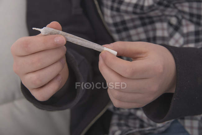 Close-up of marijuana cigarette in hands of teenager. — Stock Photo