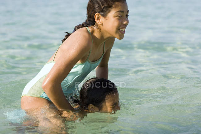 Chica en los hombros de la hermana jugando y empujando hacia el mar . - foto de stock