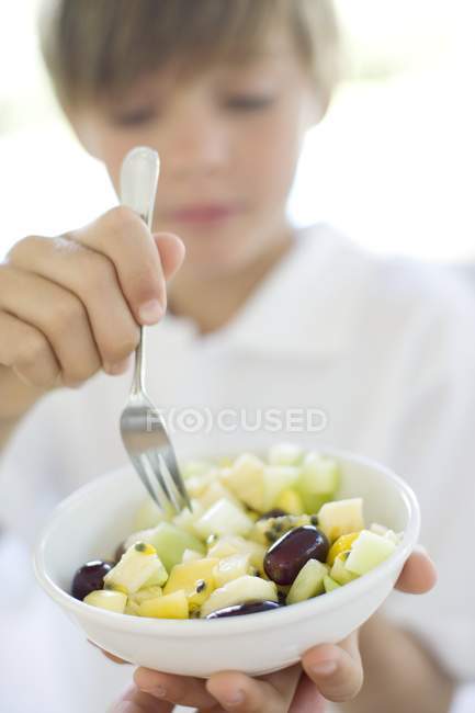 Età elementare ragazzo mangiare macedonia di frutta in ciotola . — Foto stock