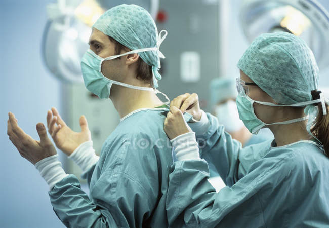 Enfermeira assistindo cirurgião e amarrando roupas protetoras . — Fotografia de Stock