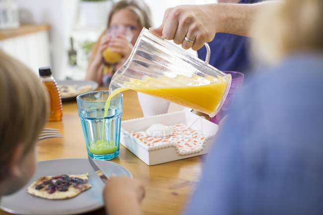Father pouring orange juice from jug at breakfast. — Stock Photo