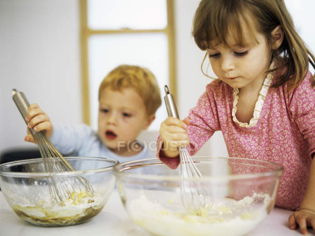 Дошкольные братья и сёстры смешивают яйца, сахар и муку в мисках для смешивания . — стоковое фото
