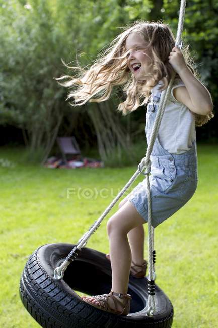 Girl playing on tire swing in garden. — Stock Photo