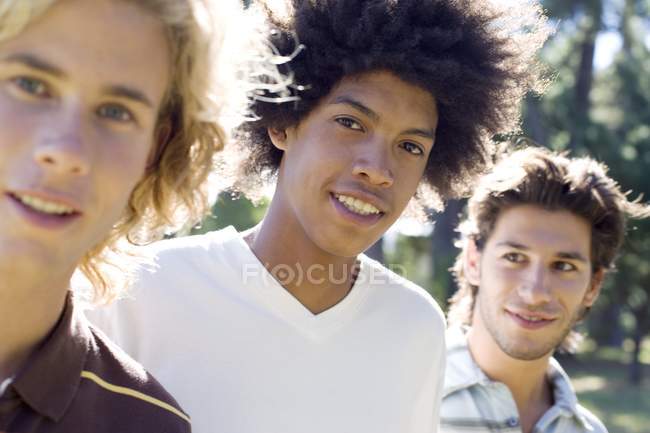 Drei junge männliche Freunde hängen im Park herum und lächeln. — Stockfoto
