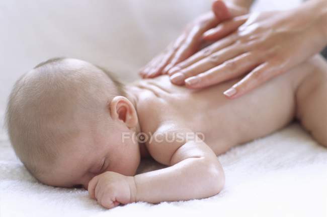 Weibliche Hände massieren Rücken eines neugeborenen Jungen. — Stockfoto