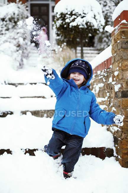 Menino da idade elementar em roupas de inverno brincando na rua com neve . — Fotografia de Stock