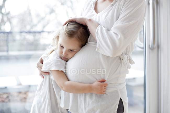 Menina abraçando mãe grávida e olhando para longe . — Fotografia de Stock