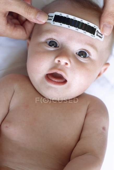 Manos femeninas presionando el termómetro de tira a la frente de niña . - foto de stock
