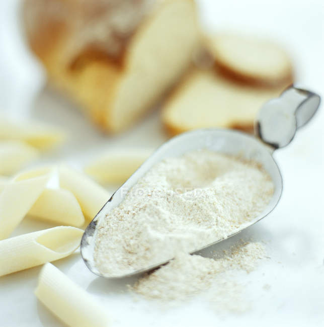 Flour in scoop with wheat pasta and bread on table, close-up. — Stock Photo