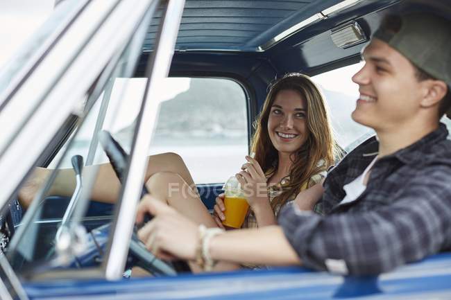 Junges Paar sitzt im Auto, während Frau Tasse mit Getränk hält. — Stockfoto