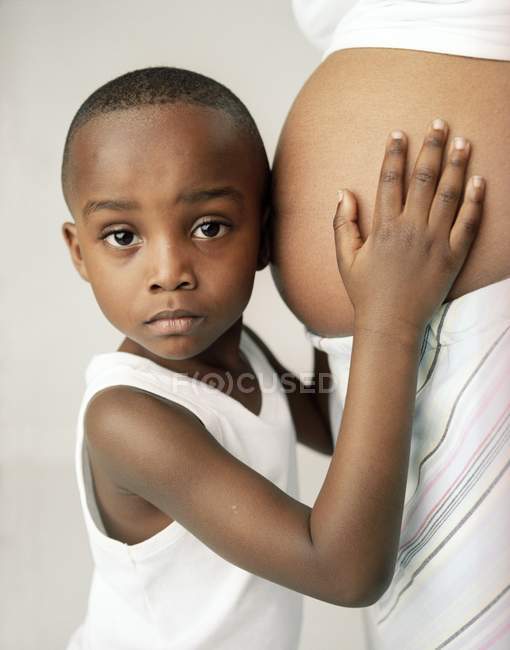 Garçon d'âge préscolaire écoutant l'abdomen gonflé de la mère enceinte
. — Photo de stock