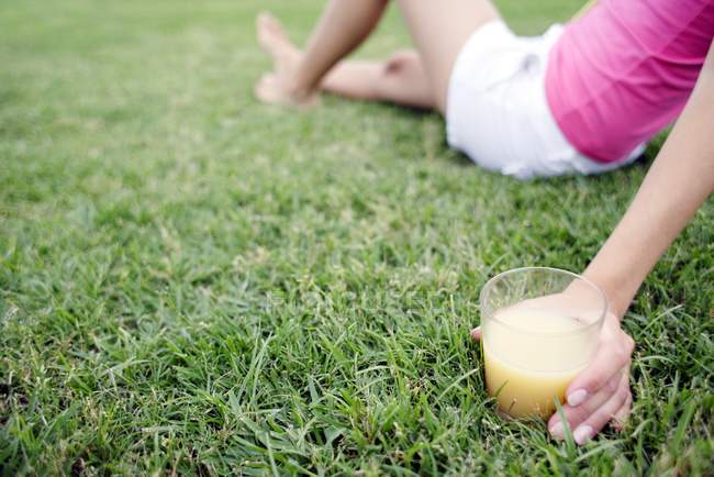 Frau sitzt mit Glas Fruchtsaft auf Gras. — Stockfoto