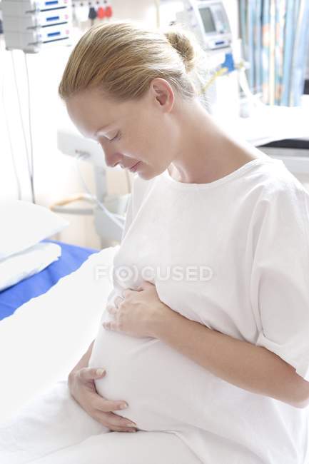 Pregnant woman at maternity ward holding swollen abdomen. — Stock Photo