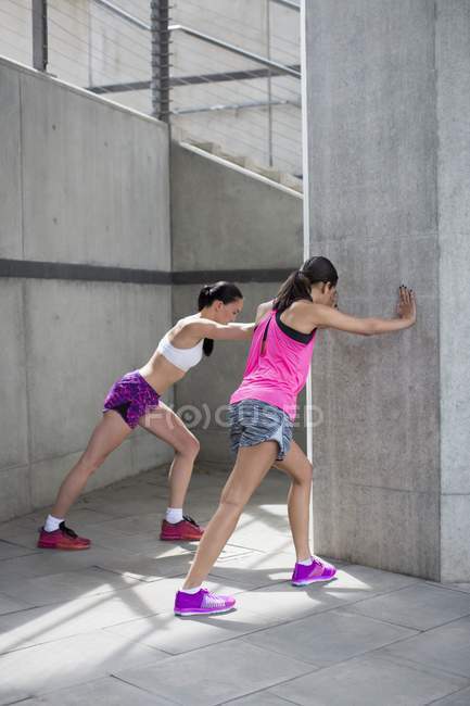 Young women stretching against wall — Stock Photo