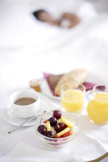 Поднос с кофе, соком и фруктами рядом со спящей женщиной . — стоковое фото