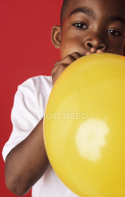 Elementary age boy blowing up yellow balloon. — Stock Photo