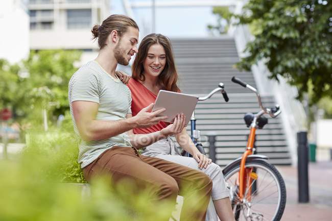 Couple sitting on street wall with digital tablet. — Stock Photo