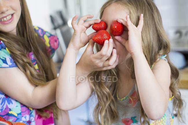 Girl helping sister covering eyes with strawberries. — Stock Photo