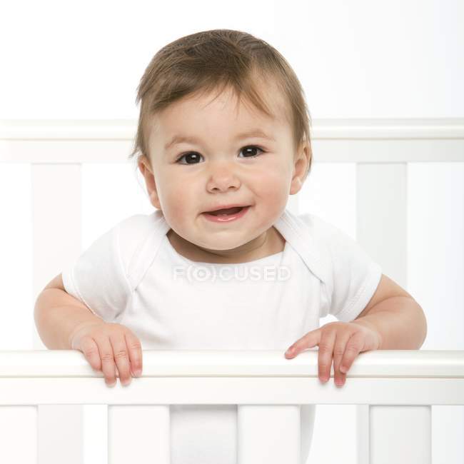 Baby girl standing in cot and looking in camera. — Stock Photo