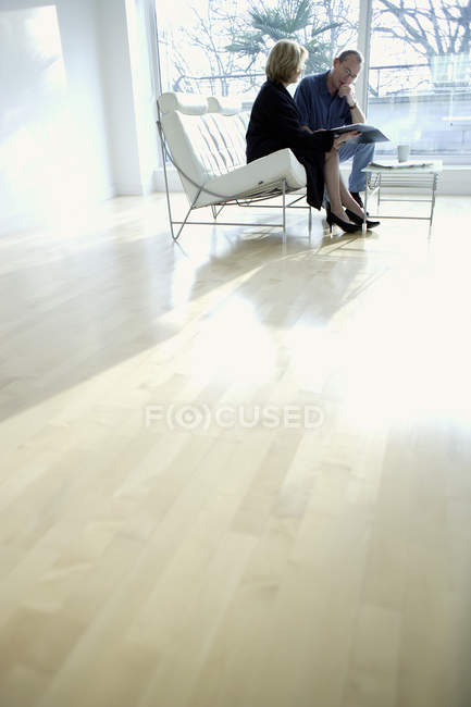 Зрелый мужчина и женщина обсуждают бизнес на белом диване в помещении . — стоковое фото