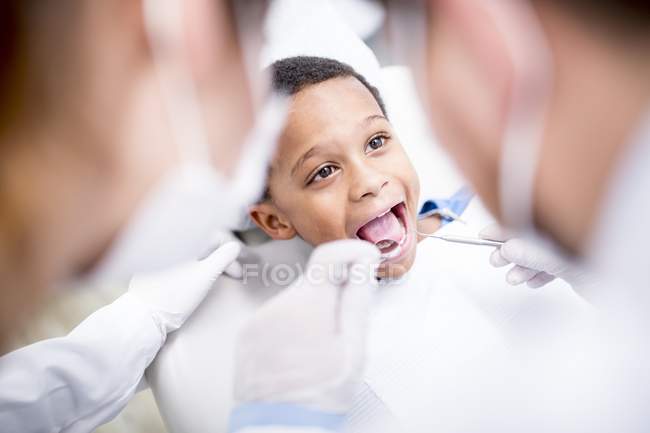 Врачи, осматривающие зубы мальчика в стоматологической клинике с зеркалом во рту . — стоковое фото