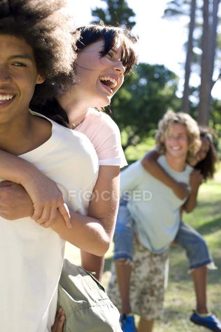 Jovens casais se divertindo no parque, homens dando mulheres piggyback equitação . — Fotografia de Stock