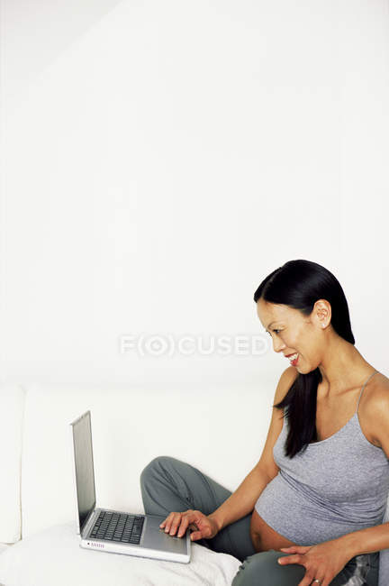 Вагітна жінка використовує ноутбук на ліжку . — стокове фото