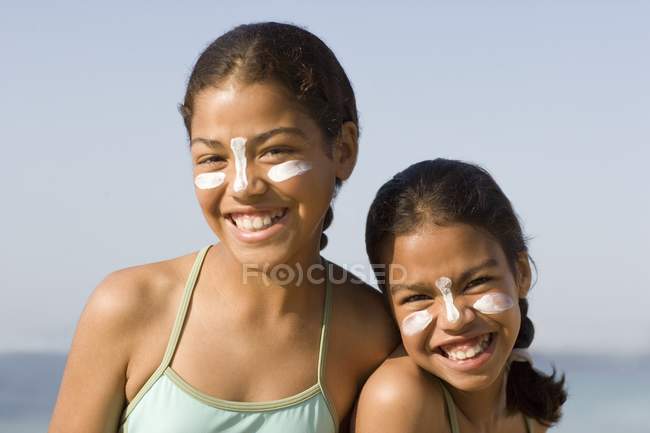 Sisters with sun cream on faces on beach. — Stock Photo