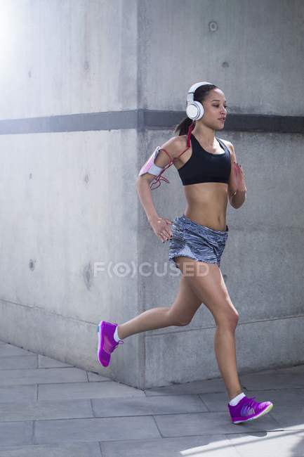 Jovem mulher usando fones de ouvido correndo — Fotografia de Stock