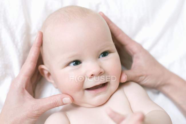 Las manos femeninas masajeando la cabeza del bebé . - foto de stock