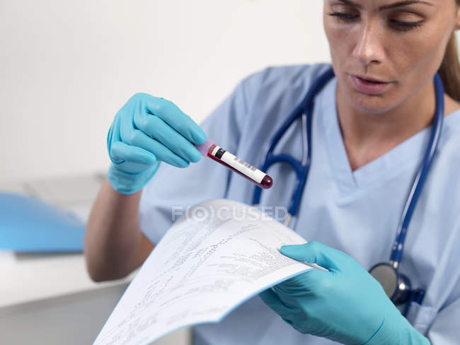 Médico leyendo los resultados del análisis de sangre mientras sostiene la muestra de sangre . - foto de stock