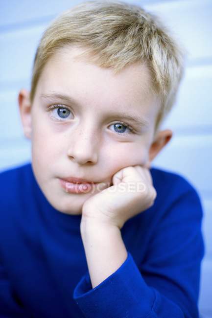 Retrato de menino pensativo em camiseta azul com a mão no queixo . — Fotografia de Stock