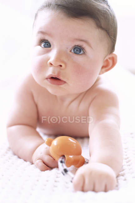 Baby boy lying on front and holding toy. — Stock Photo