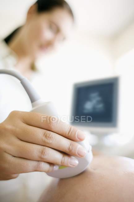 Obstetrician using ultrasound transducer for scanning abdomen of pregnant woman. — Stock Photo