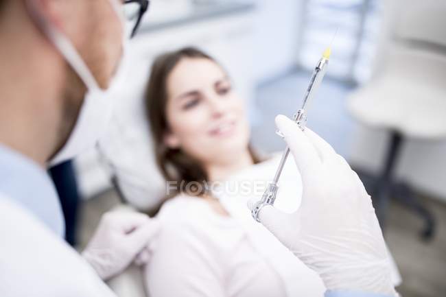 Dentista segurando seringa com paciente na clínica odontológica . — Fotografia de Stock