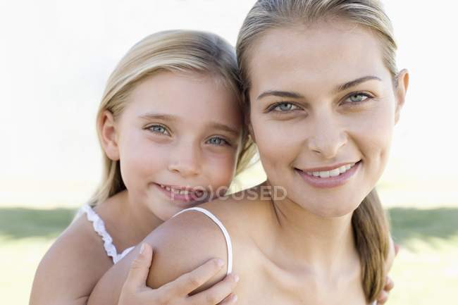Mother carrying daughter on back and looking in camera. — Stock Photo
