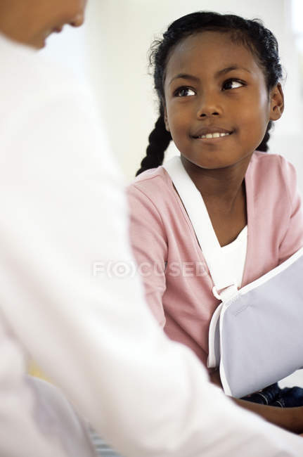 Ärztin spricht Mädchen mit verletztem Arm im Tragetuch an. — Stockfoto