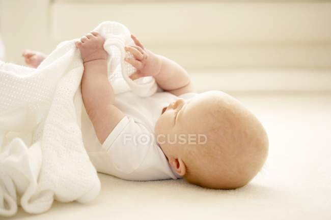 Baby girl playing with blanket on floor. — Stock Photo