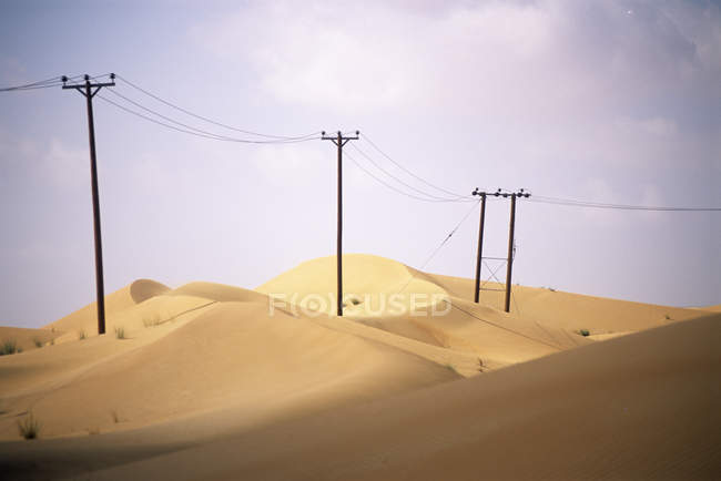 Piloni in legno che supportano le linee elettriche attraverso dune di sabbia negli Emirati Arabi Uniti
. — Foto stock
