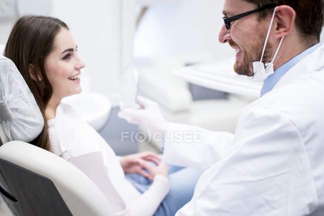 Dentista e paziente che parlano e sorridono in clinica dentale . — Foto stock