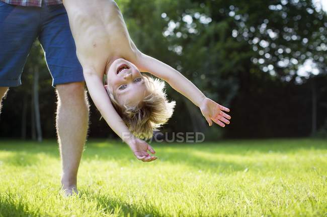 Padre sosteniendo al hijo boca abajo en el jardín . - foto de stock